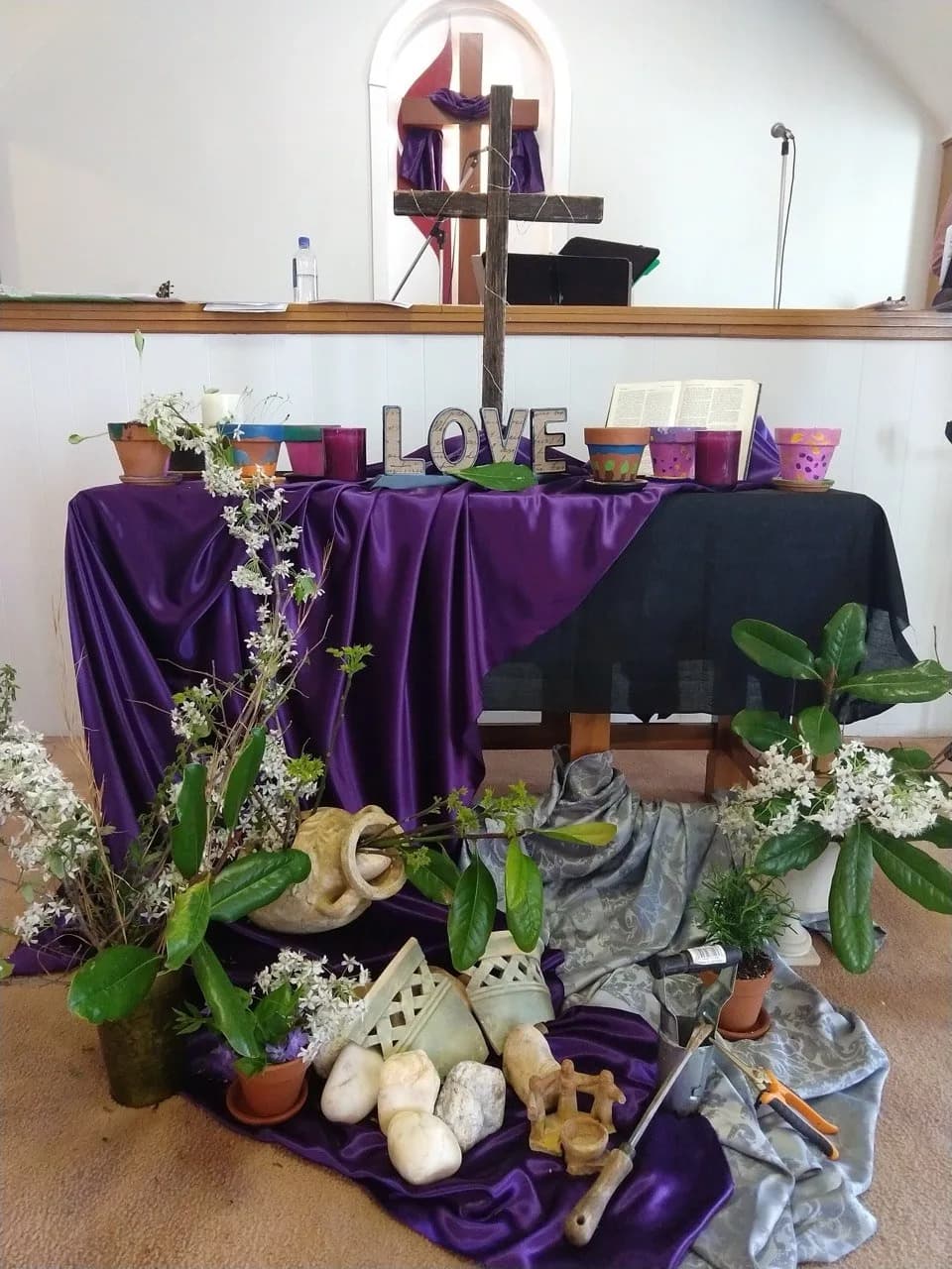 Altar table at Weaver First UMC decorated with purple fabric, LOVE sign, white flowering branches, and stones — Candy Sefcik's garden table